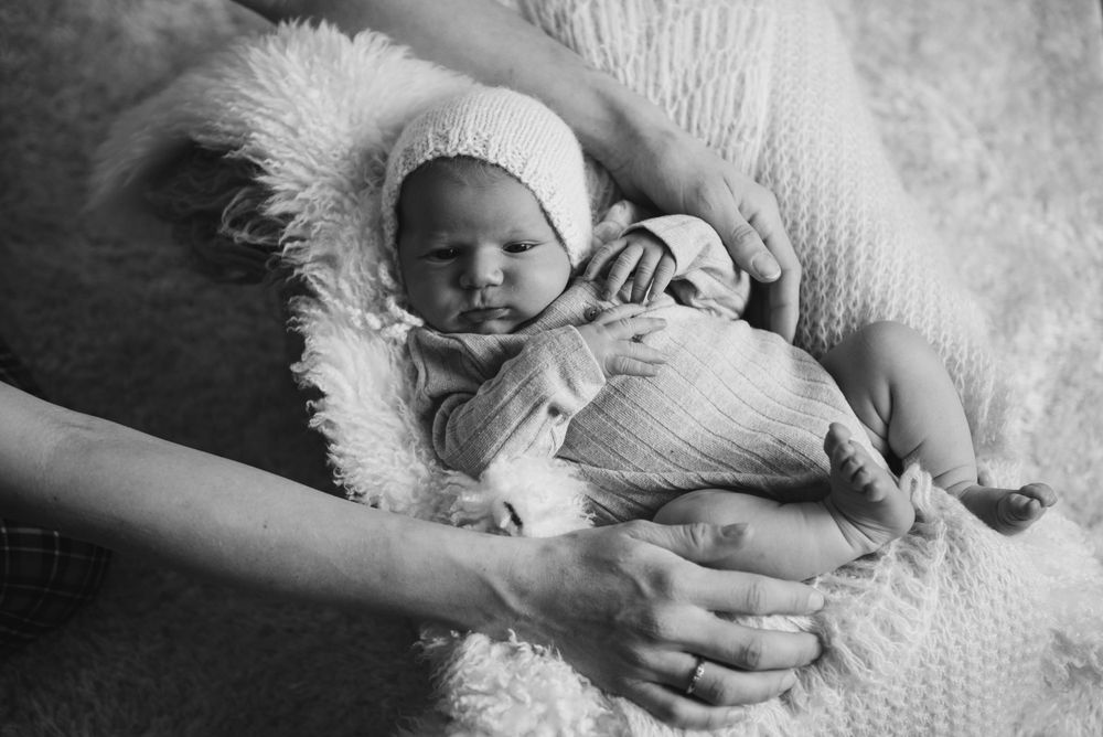 Black and white image of newborn resting on soft white fur blanket.