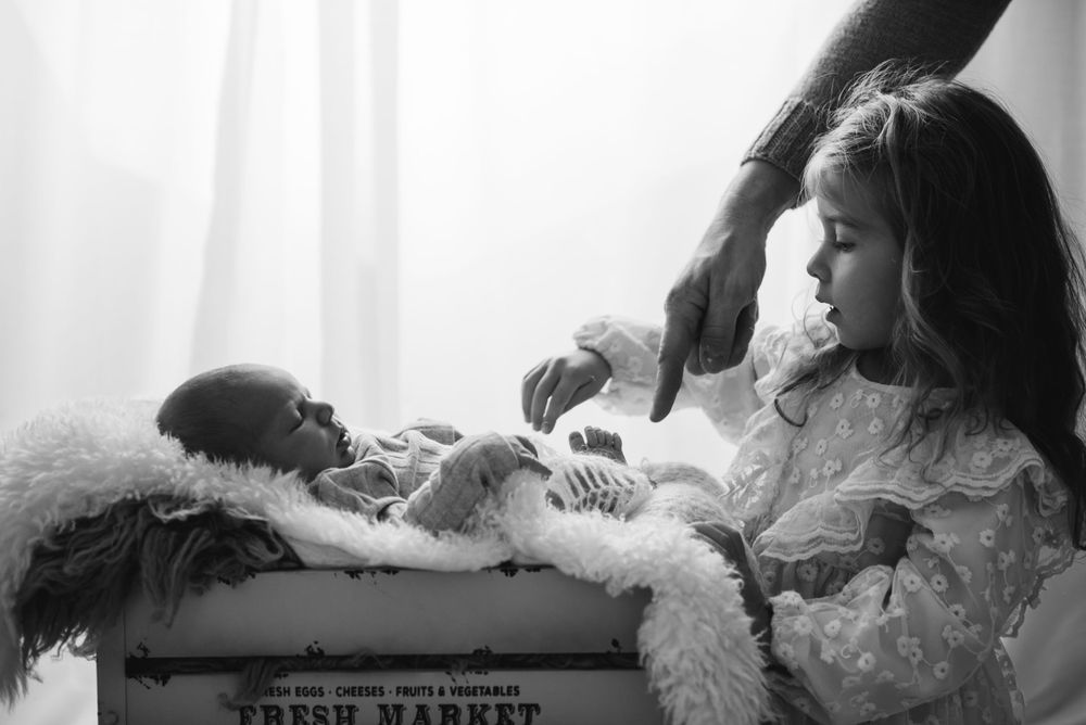 Black and white photograph of nurturing moment with baby on white blanket.