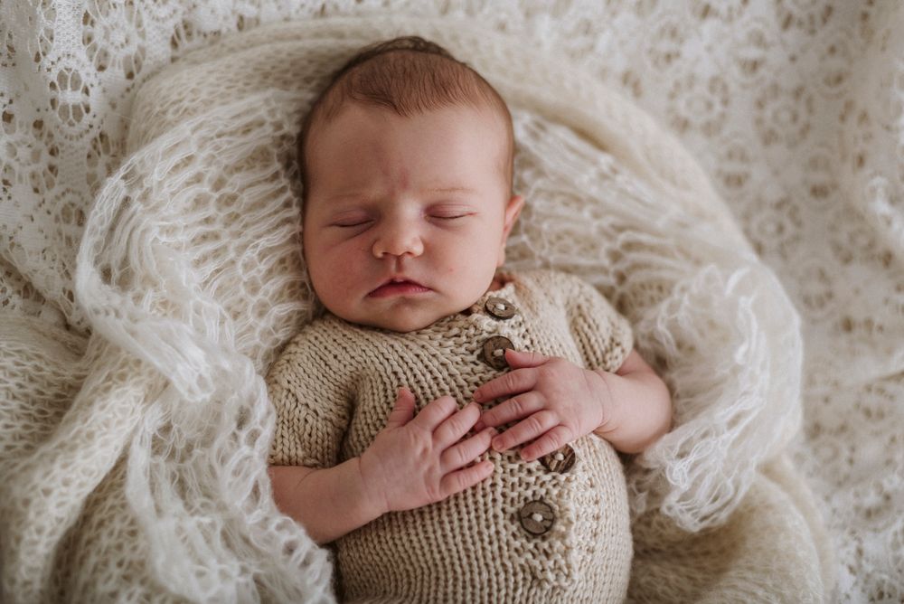 Sleeping newborn wearing knit sweater on cozy white blanket.