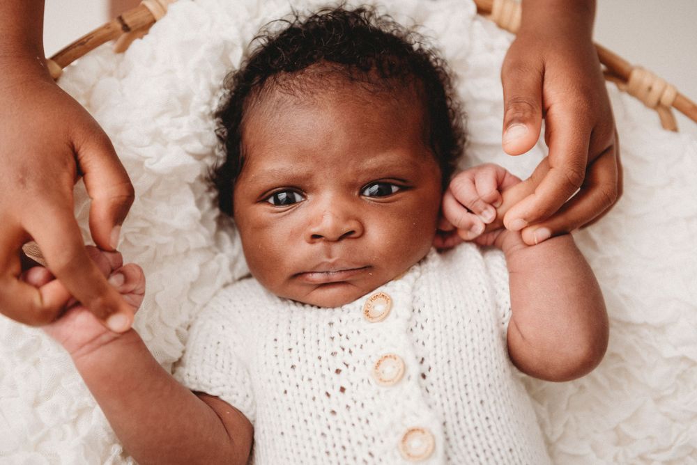 Baby wearing white knit sweater with buttons reaching out with tiny hands.