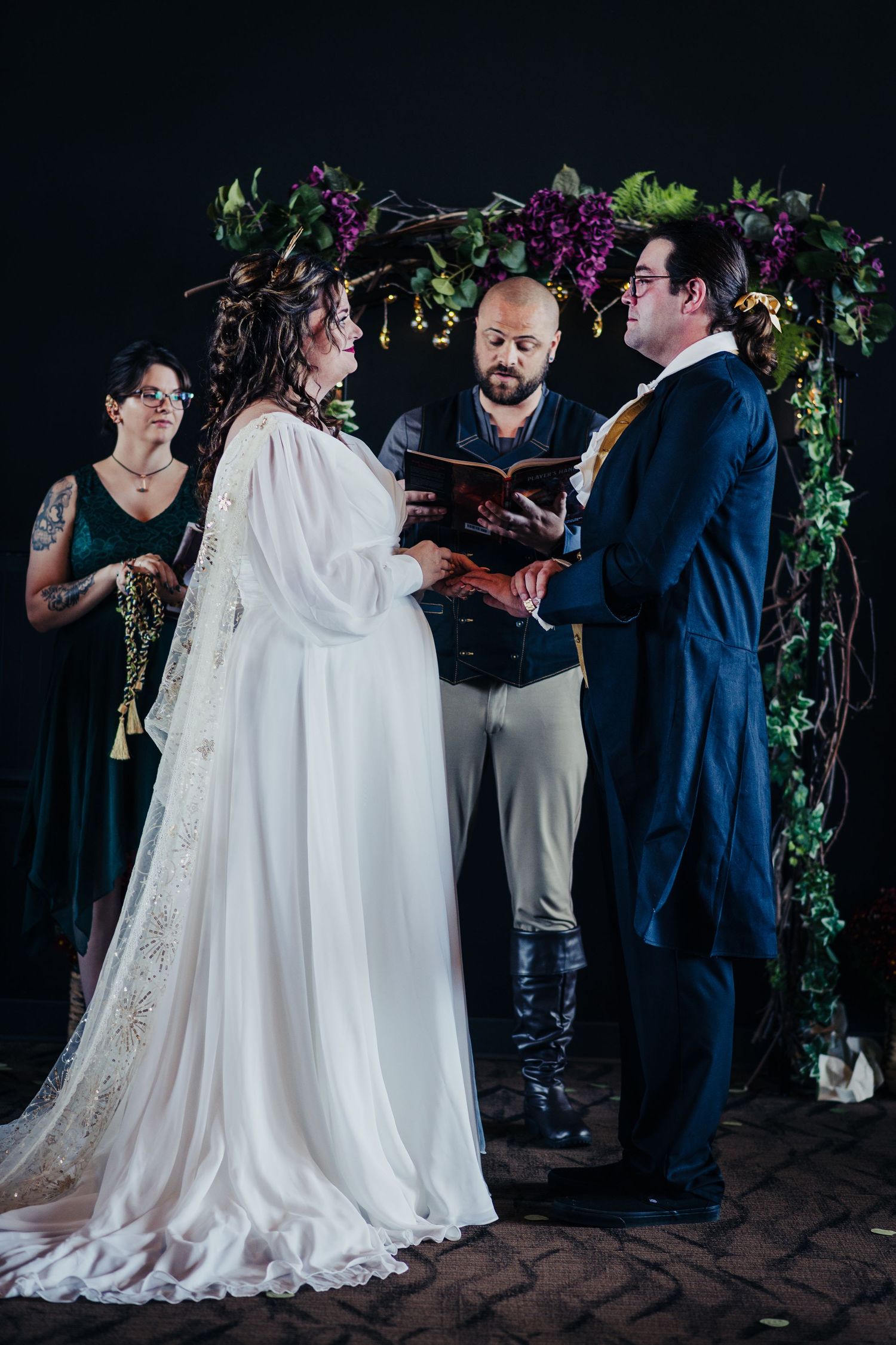 A wedding ceremony under a floral arch with dark purple and green flowers.