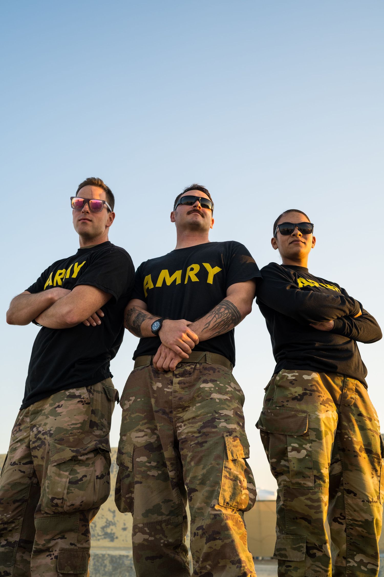 Three U.S. Army soldiers in black ARMY t-shirts and camo pants pose confidently with arms crossed.