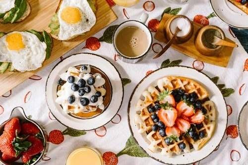 Overhead view of a breakfast spread with waffles, sunny side up eggs, berries, and coffee on a patterned tablecloth.
