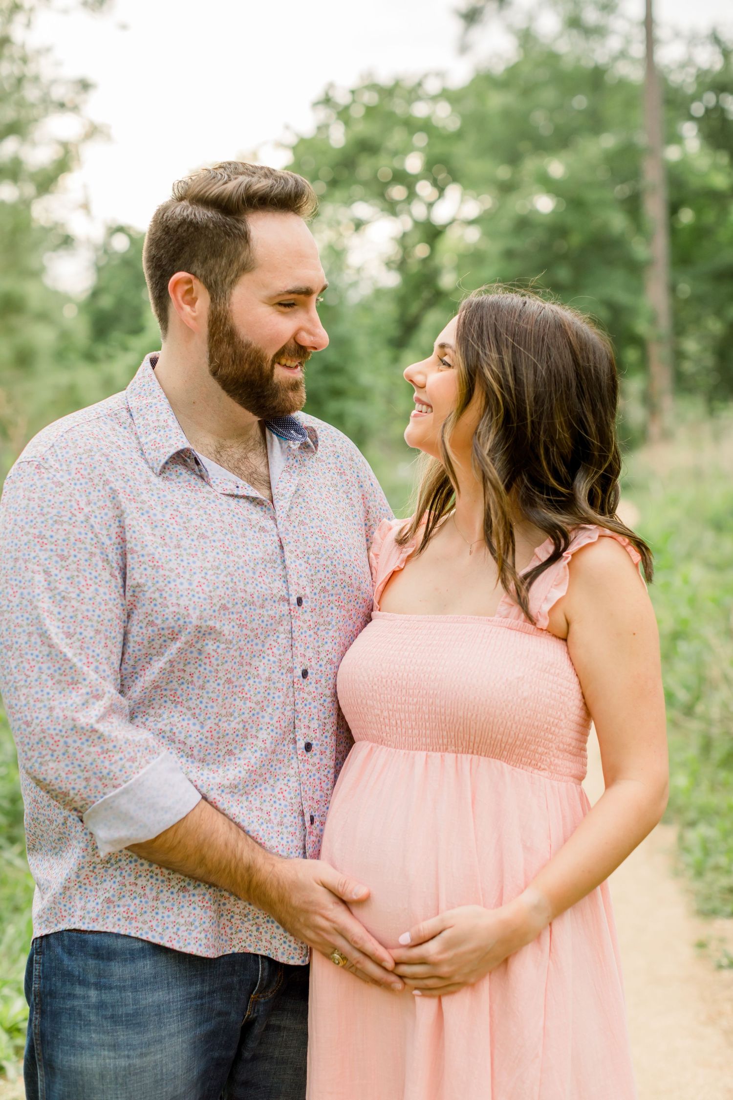 A couple laughs together during their maternity photo session on a forest path.