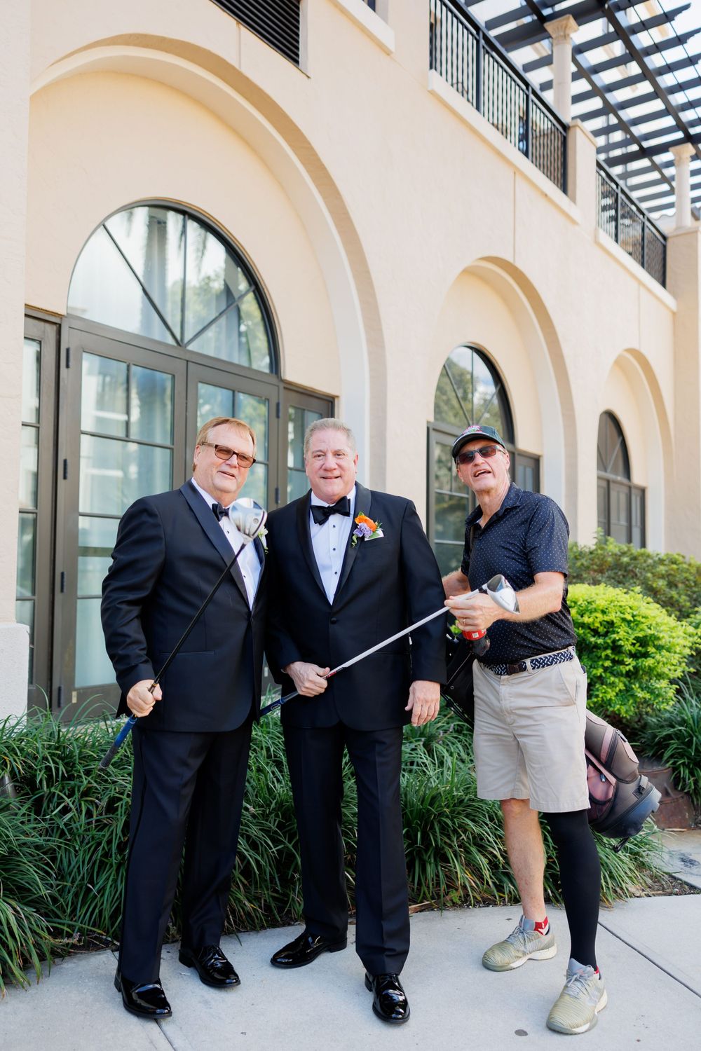 Three people stand together outside an arched building, with one holding photography equipment.