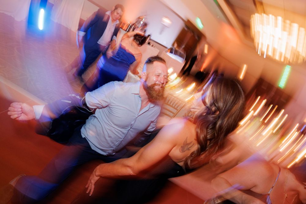 Motion-blurred photograph capturing the energy of dancing wedding guests under warm lighting.