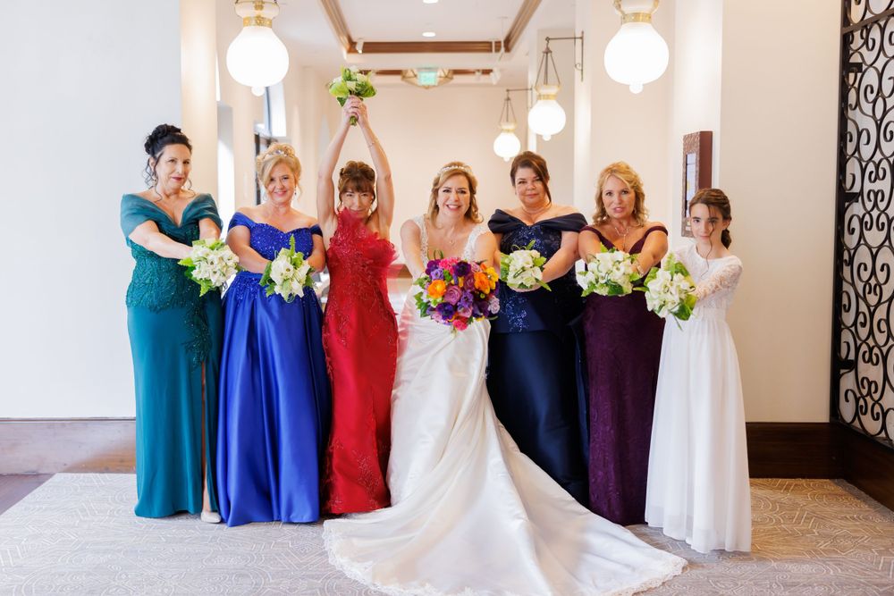 A bride in a flowing white dress with a long train holds a vibrant bouquet in an elegant venue.