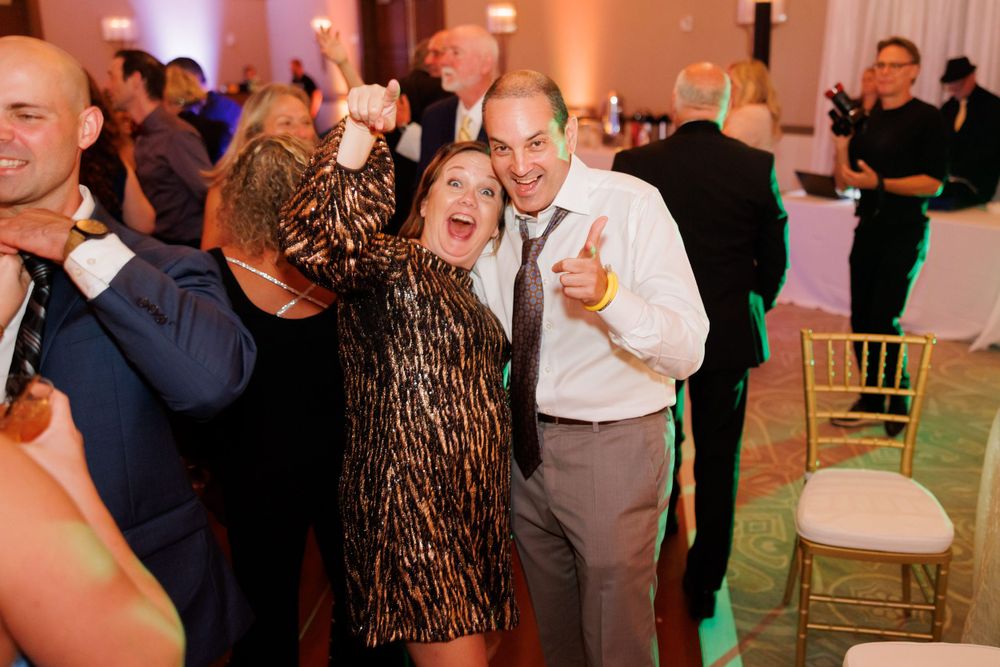 Wedding guests dancing and laughing together during a lively reception celebration.