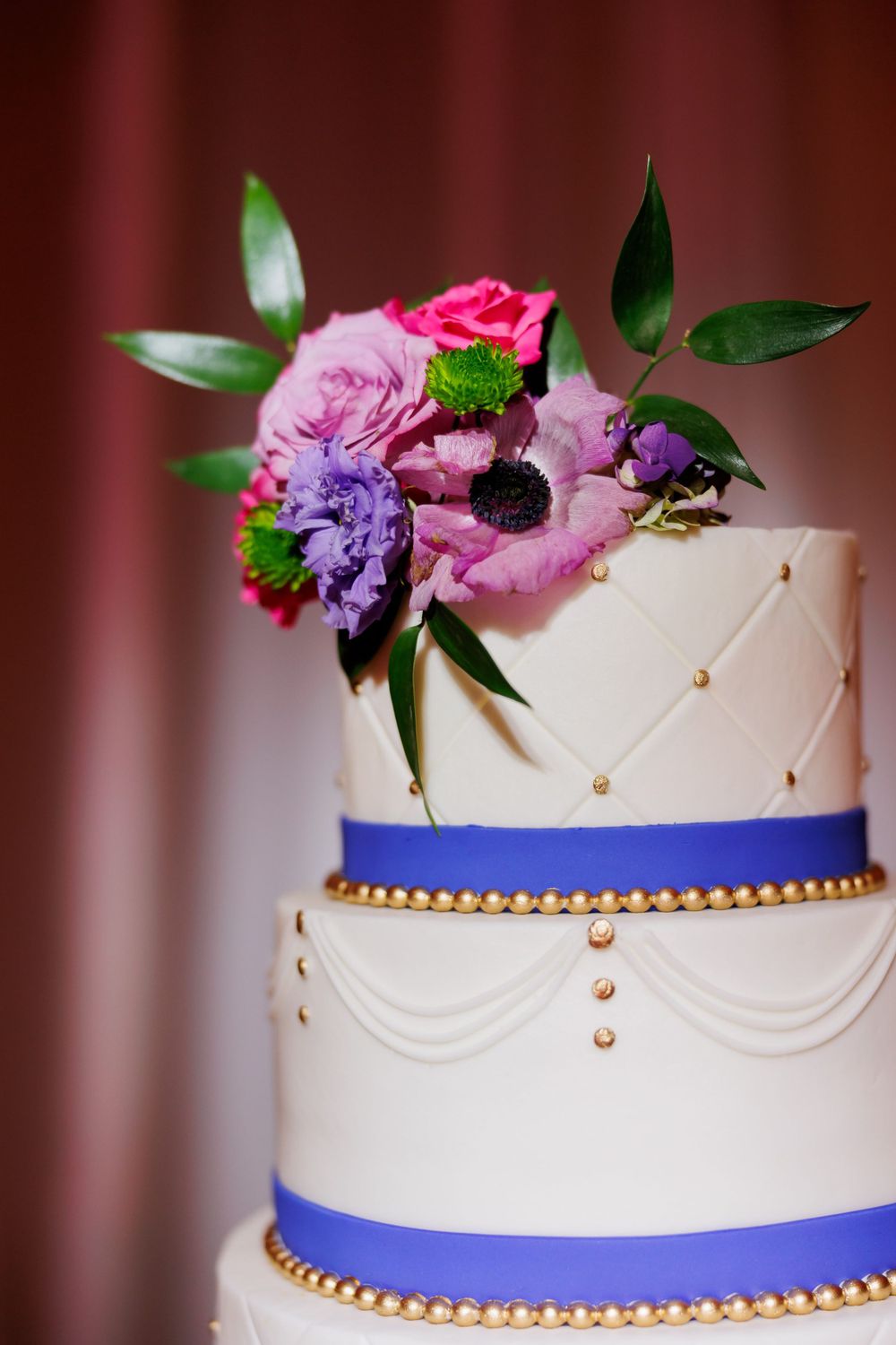 Close-up of wedding cake detail showing white frosting, blue ribbon, and fresh pink and purple flowers.