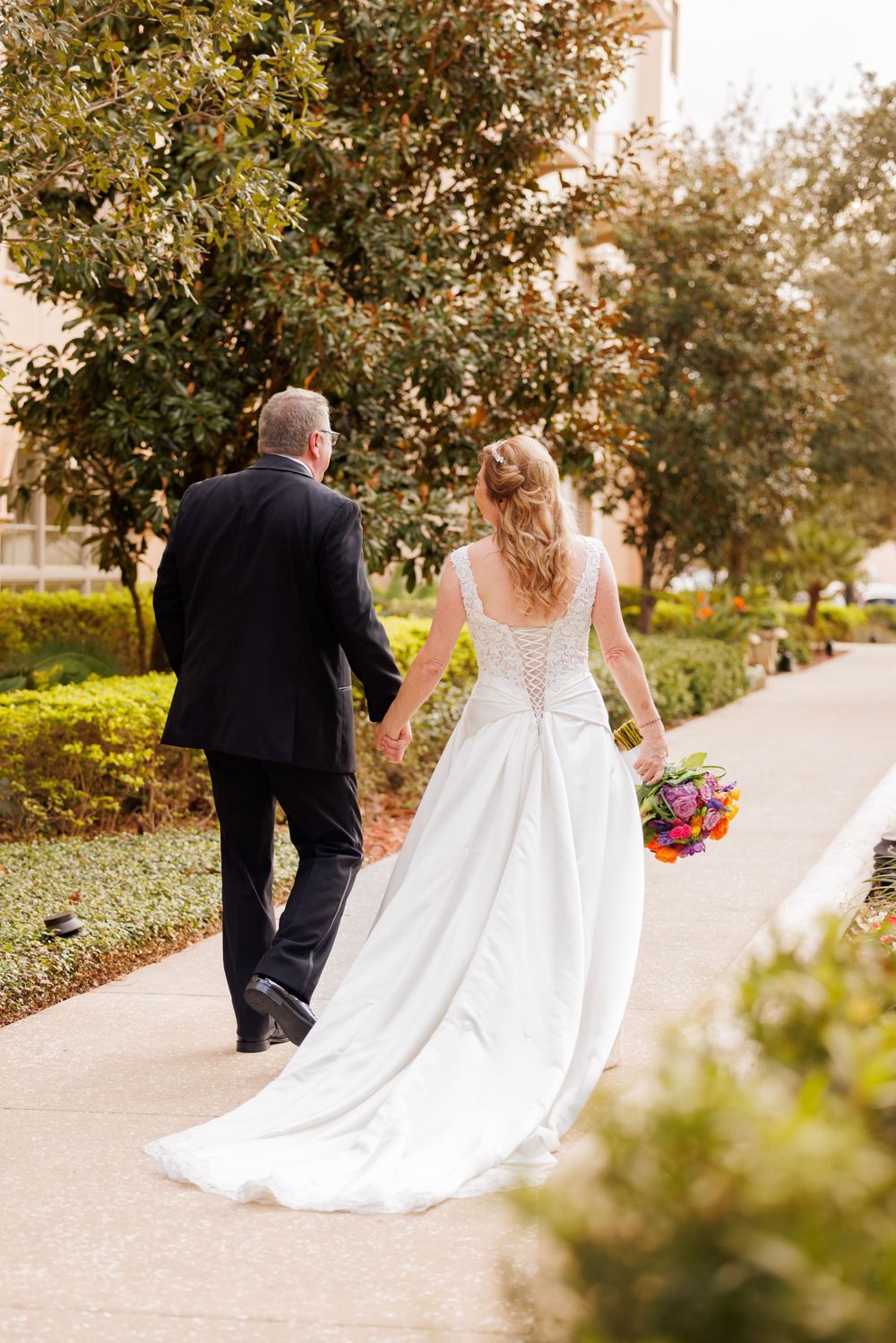 White wedding dress with flowing train captured on garden pathway during outdoor portrait session.
