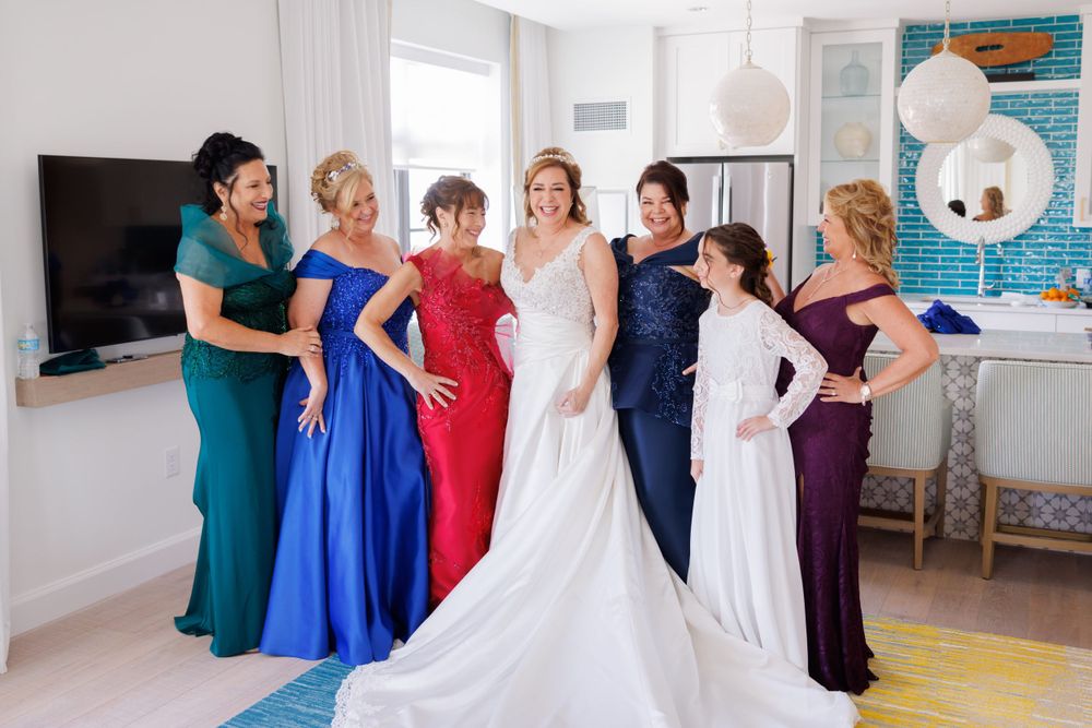 A wedding party lineup showcasing colorful floor-length gowns in an elegant hallway with pendant lighting.