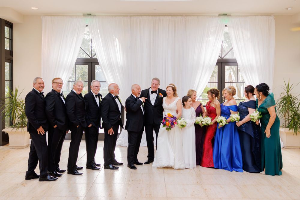 Formal wedding party portrait with black tuxedos and vibrant jewel-toned bridesmaid dresses.