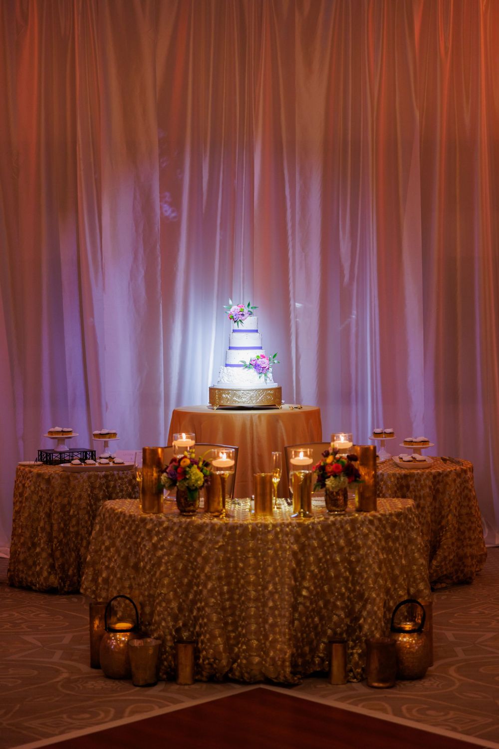 Wedding cake display table with candlelight and draped fabric backdrop creating romantic ambiance.