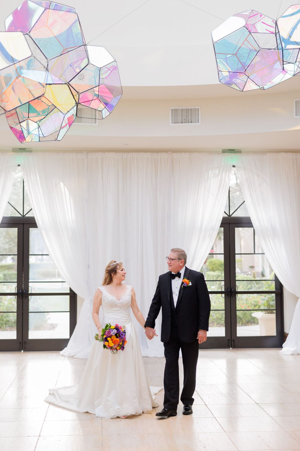 An elegant wedding venue interior featuring iridescent geometric light fixtures and white drapes.