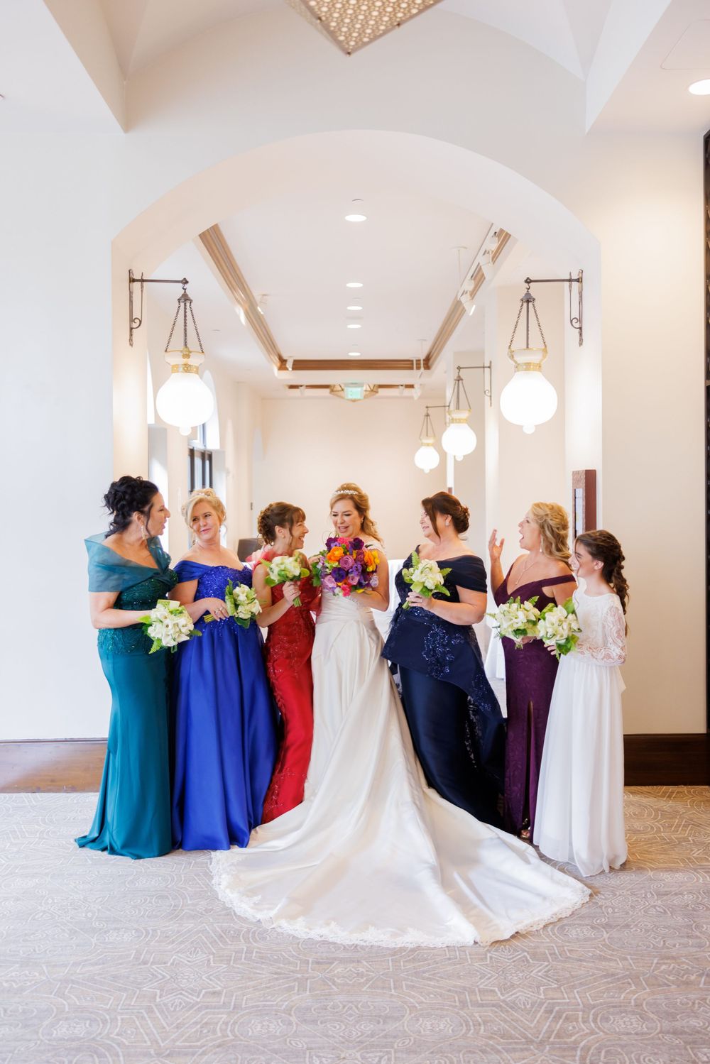 A group photo of a wedding party wearing vibrant jewel-toned dresses holding floral bouquets.