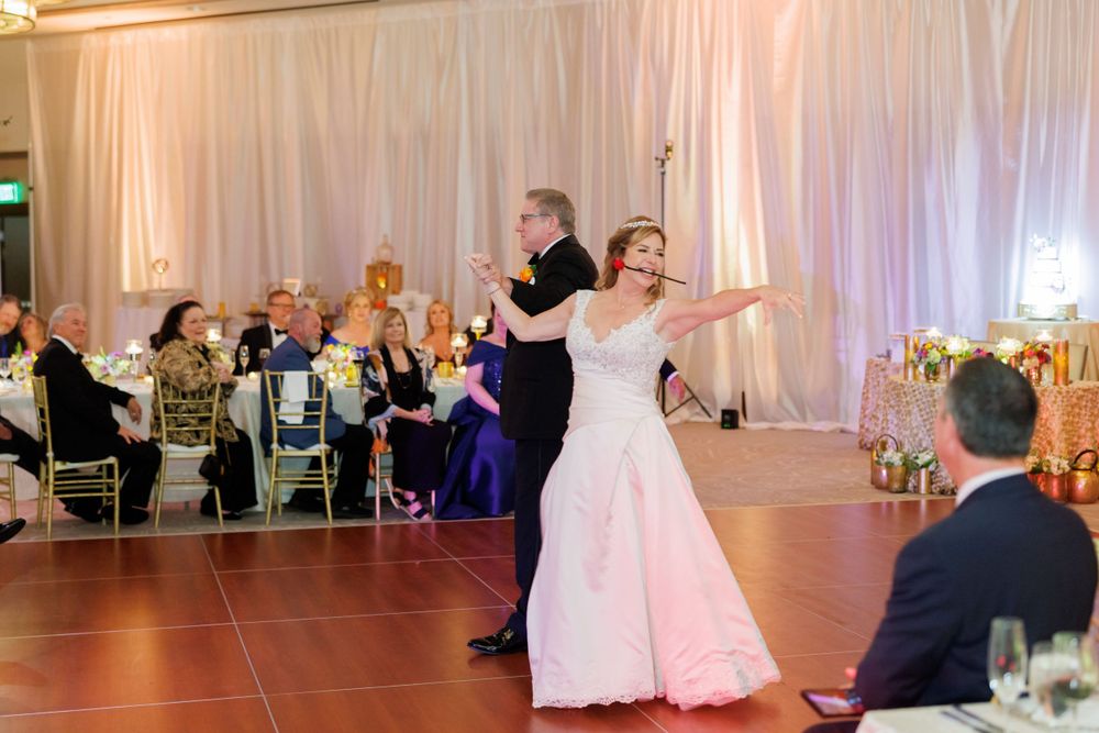 Wedding couple dancing in a ballroom decorated with white drapes and ambient lighting.