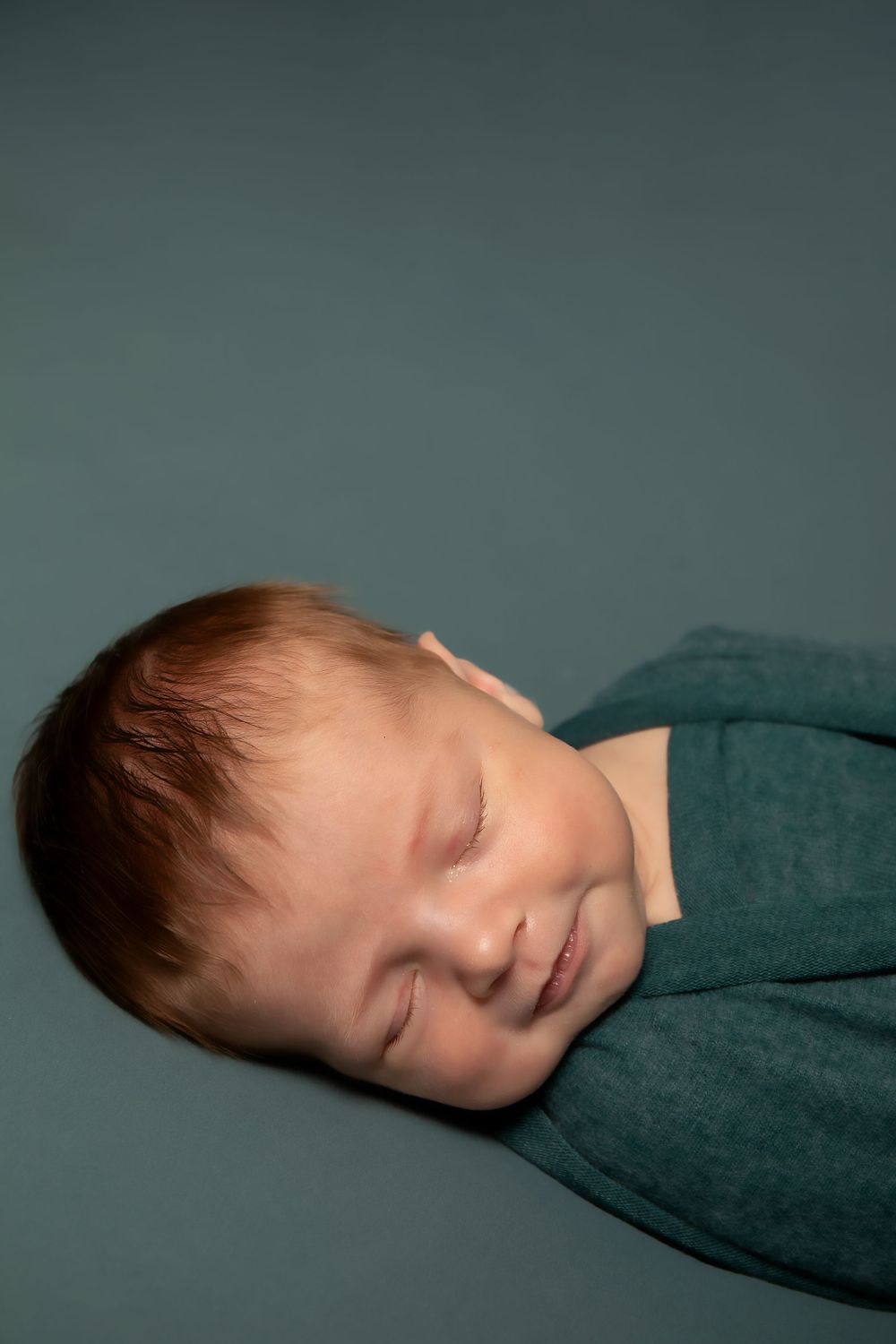 Close-up of sleeping infant against dark teal background.