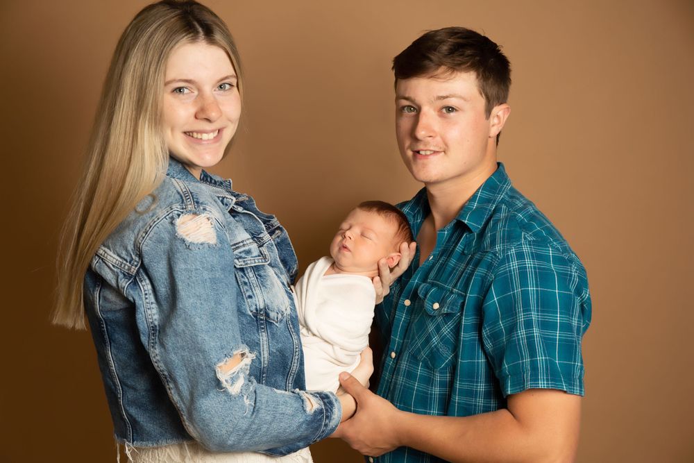 Family portrait with baby wearing white against warm brown background.