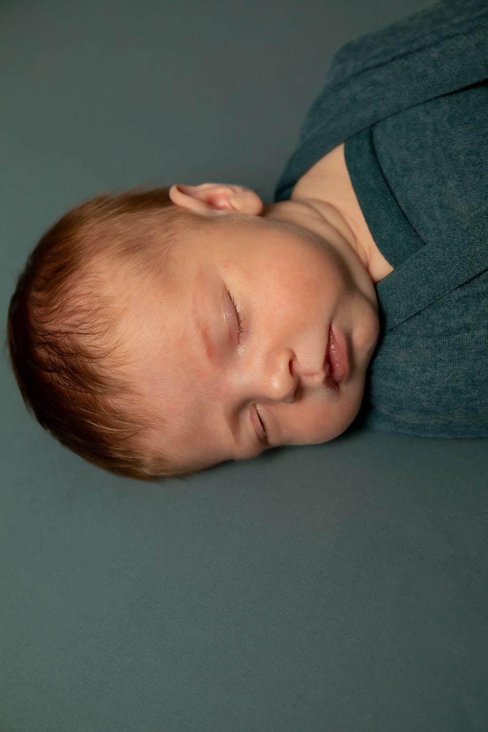 Sleeping baby with rosy cheeks against dark teal background.