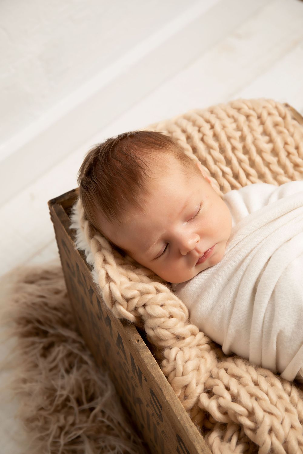 Peaceful sleeping newborn on textured knit blanket in wooden box.