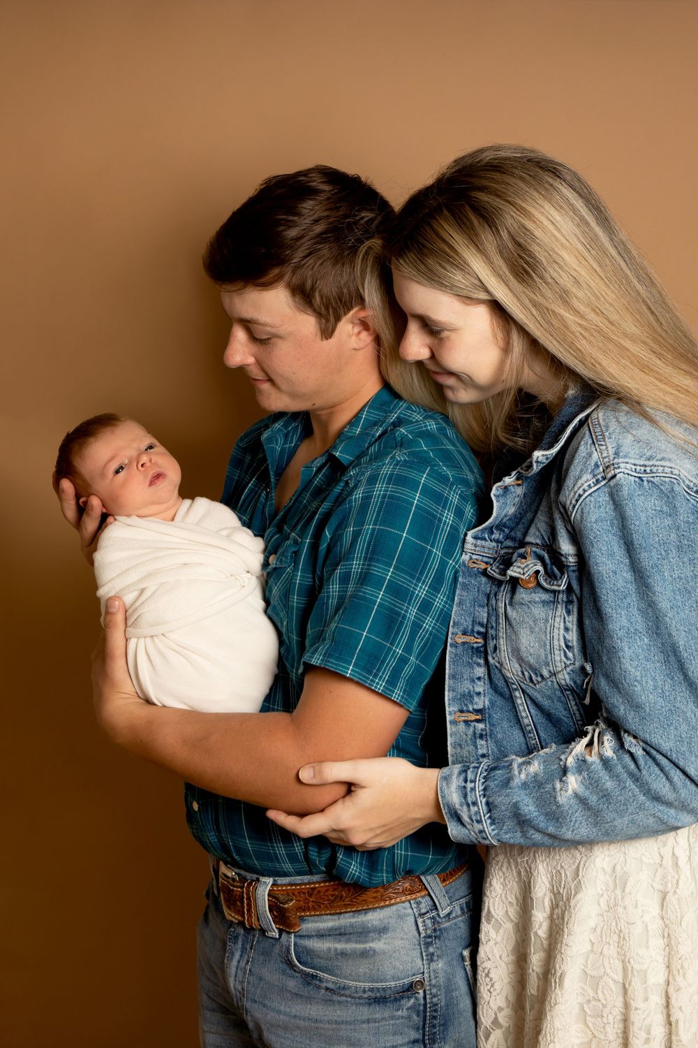 Tender family moment with newborn baby against warm brown studio background.