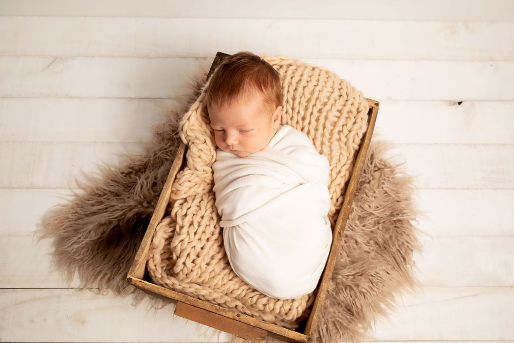 Sleeping newborn wrapped in white on chunky knit blanket with fur accents.