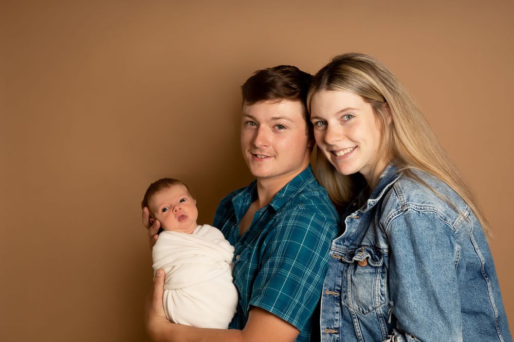 Casual family portrait with denim and plaid attire against brown backdrop.