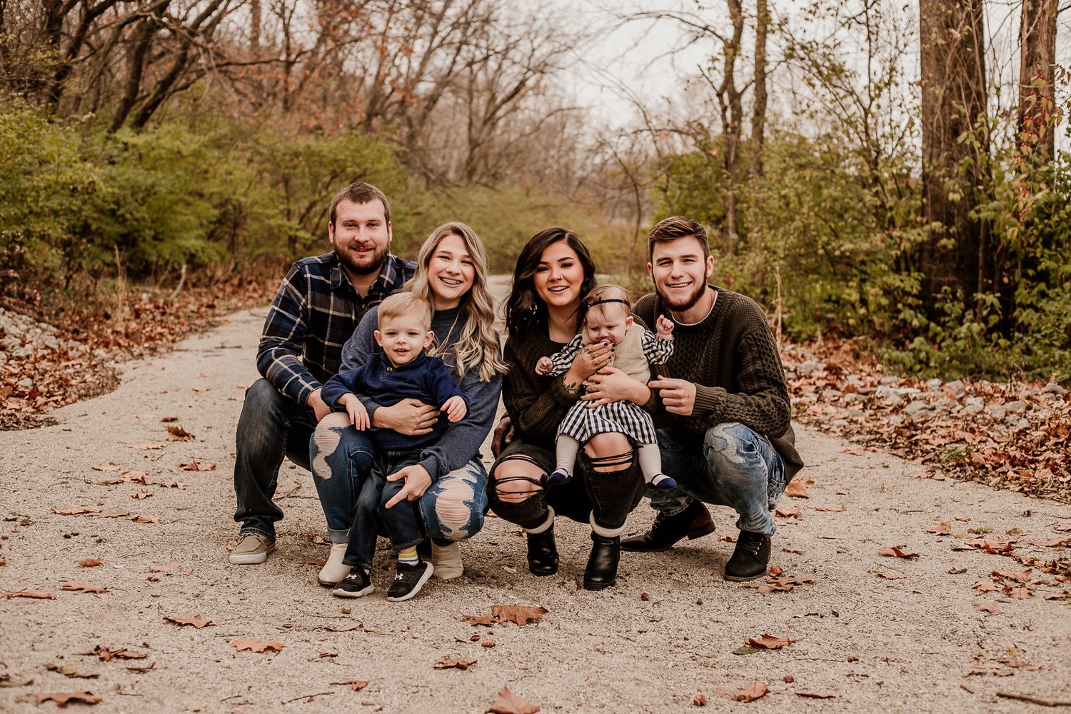 Casual outdoor family portrait taken on a wooded path during autumn.