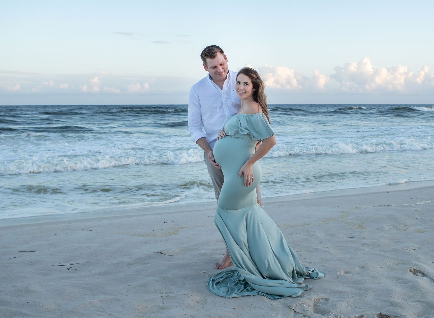 A husband and pregnant wife at maternity session in Pensacola, FL. Greens and blues in her dress and the gulf of Mexico. Beach maternity
