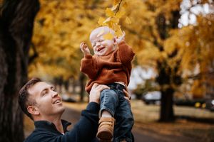 Father lifting his baby above his head to play with the yellow leaves of a tree in Salida, Colorado.