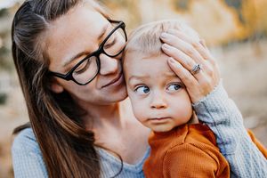 Beautiful portrait of mother kissing baby on forehead while he is looking over his shoulder.