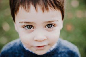 Young boy with dark hair and blue eyes gazes innocently up at Stephanie Buechler's camera during his portrait session.