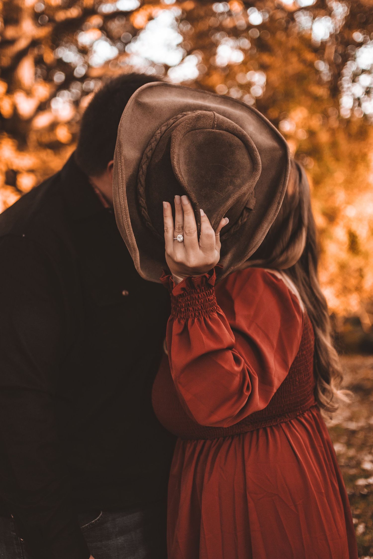 A romantic autumn scene with a figure in a red dress sharing an intimate moment under warm orange foliage.