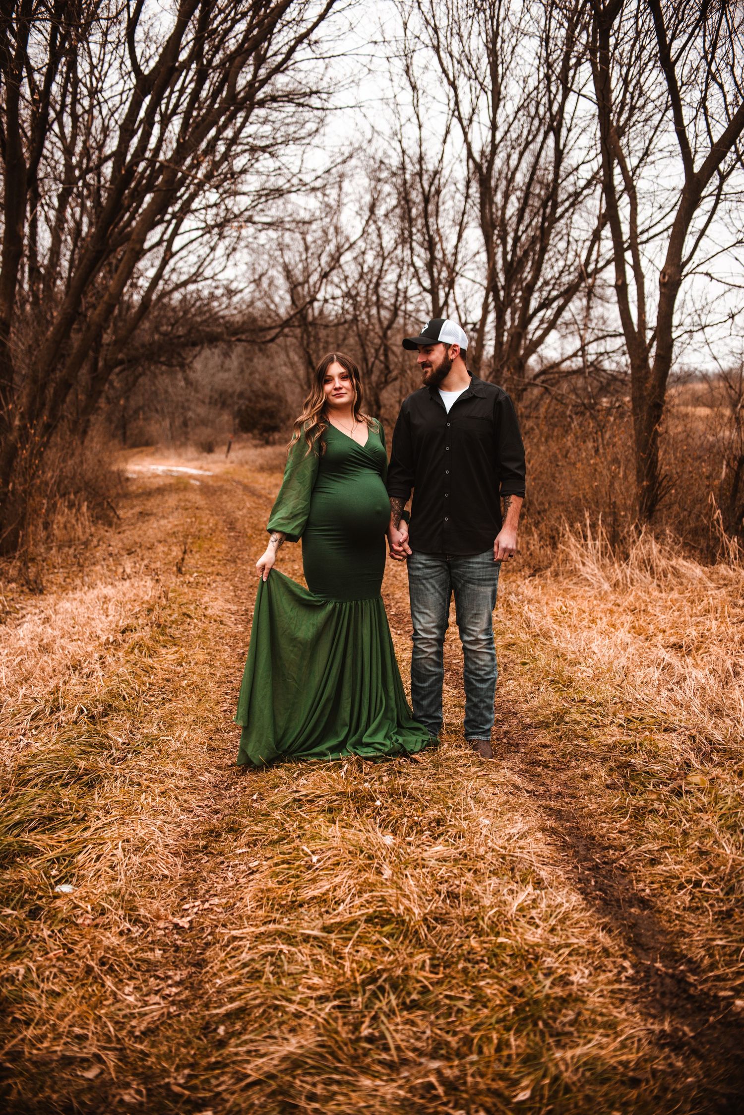 A maternity photoshoot featuring a couple in a rustic field during fall.