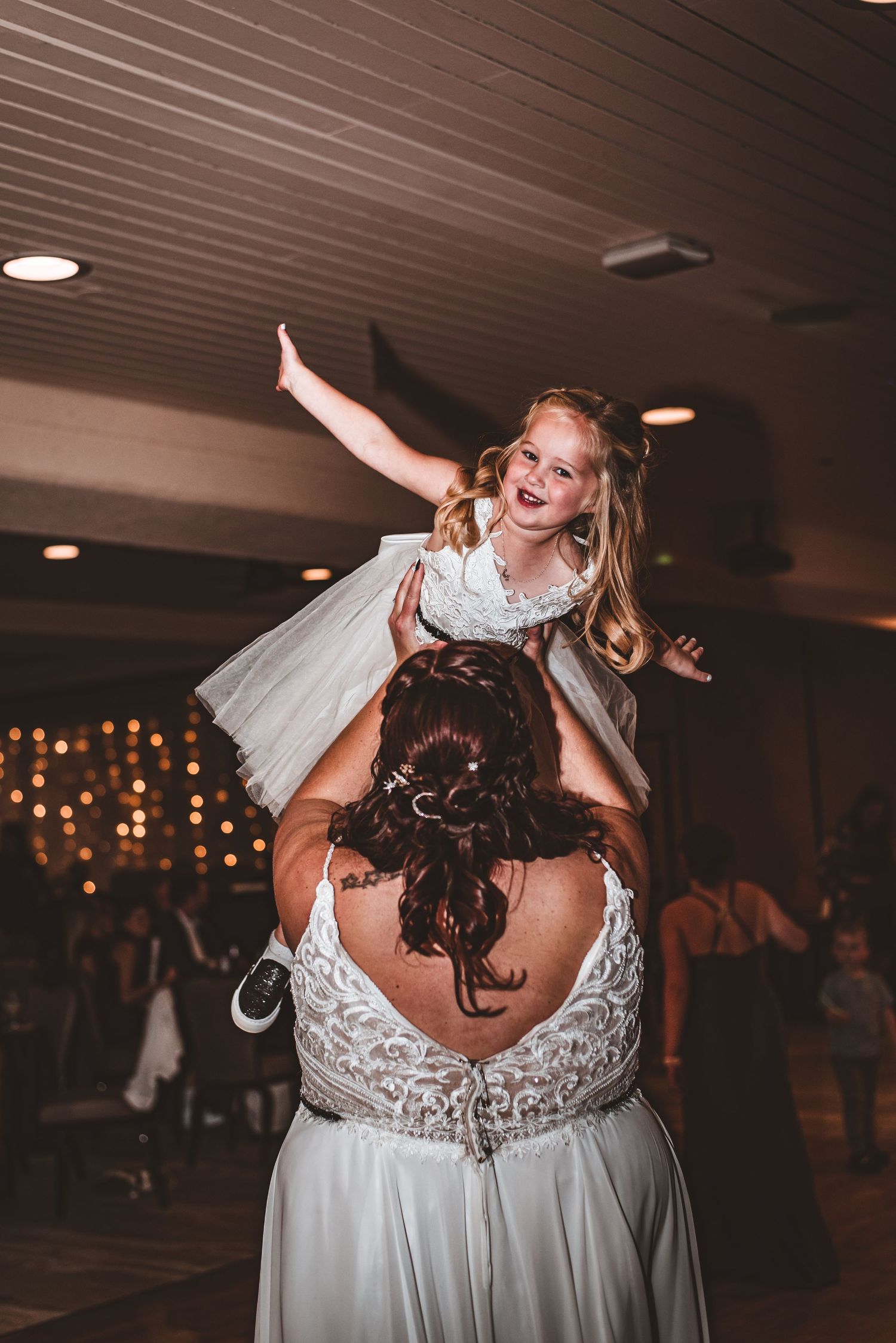 A joyful moment at a wedding reception as a child is lifted high during celebratory dancing.
