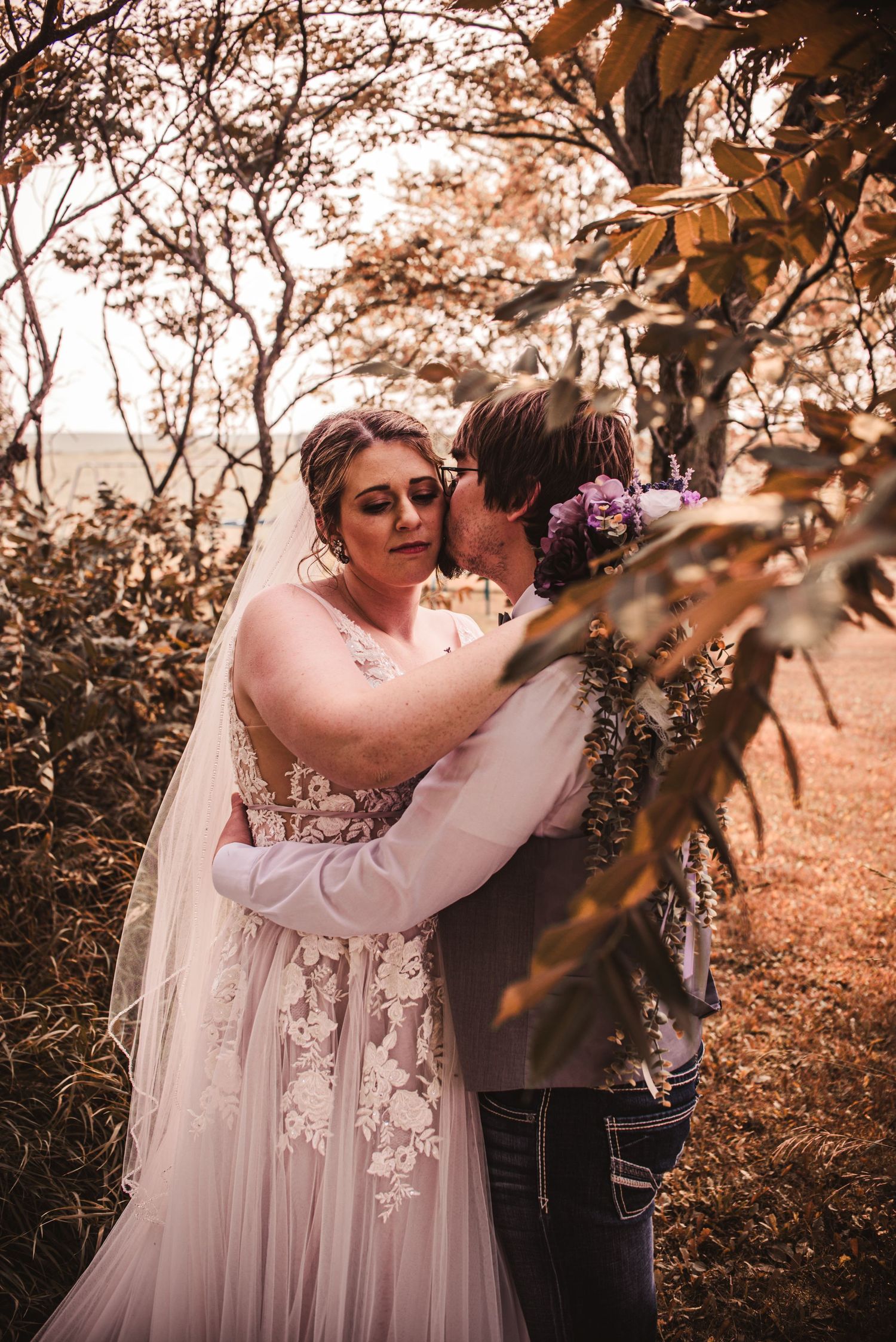 A tender wedding moment captured among autumn trees during golden hour.