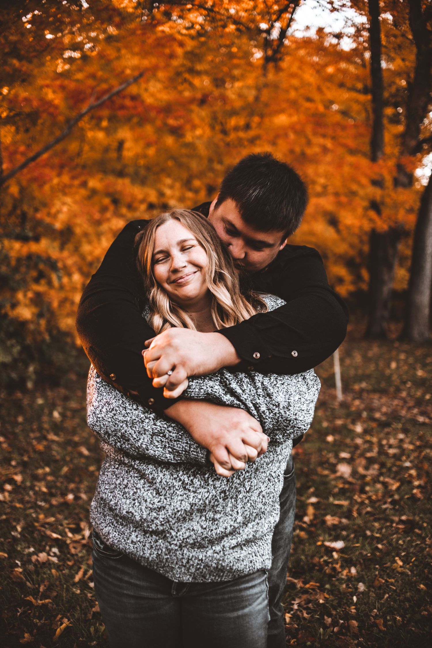 A couple embraces in an autumn forest surrounded by vibrant orange leaves.