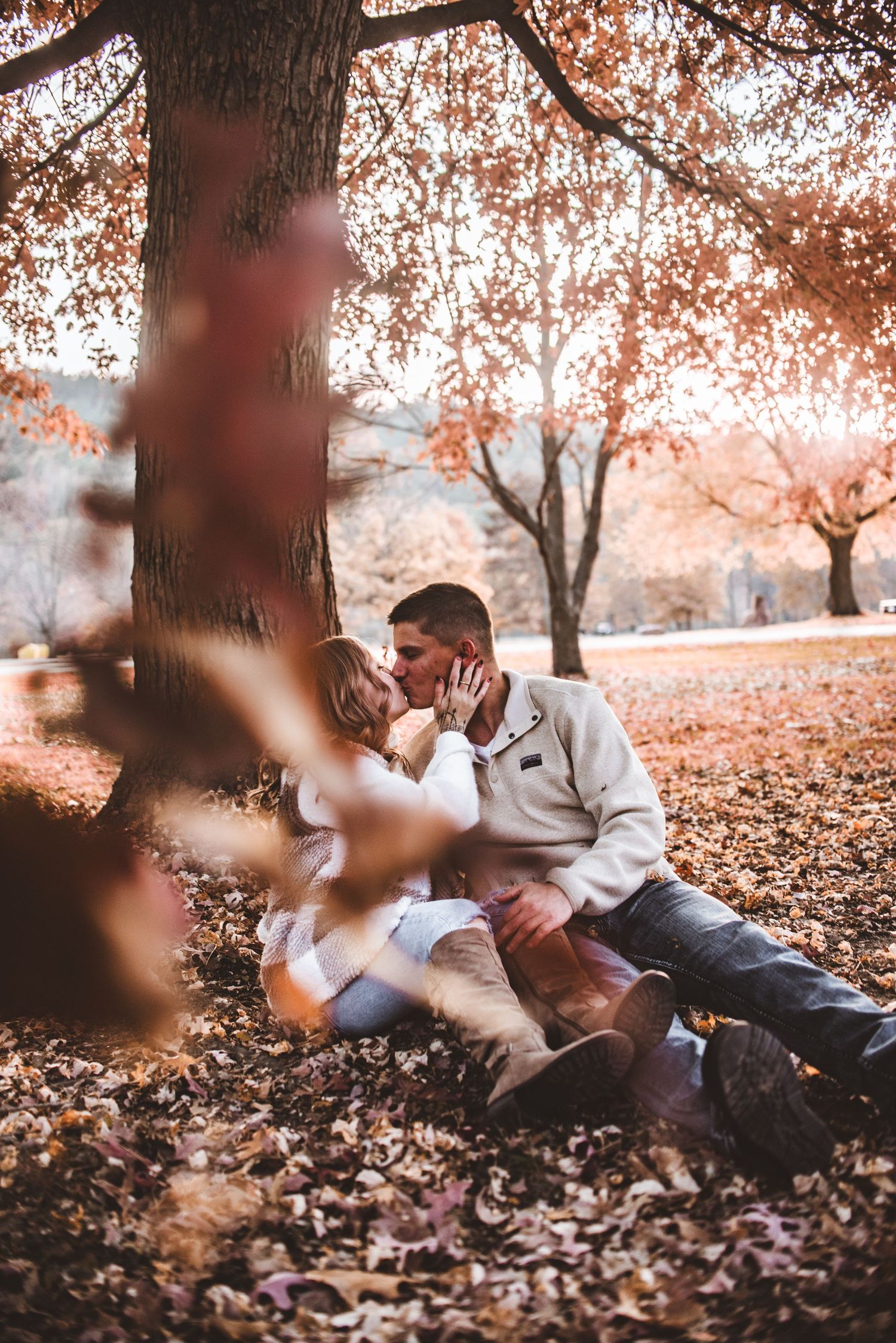 A romantic autumn moment shared beneath a tree with falling orange leaves.