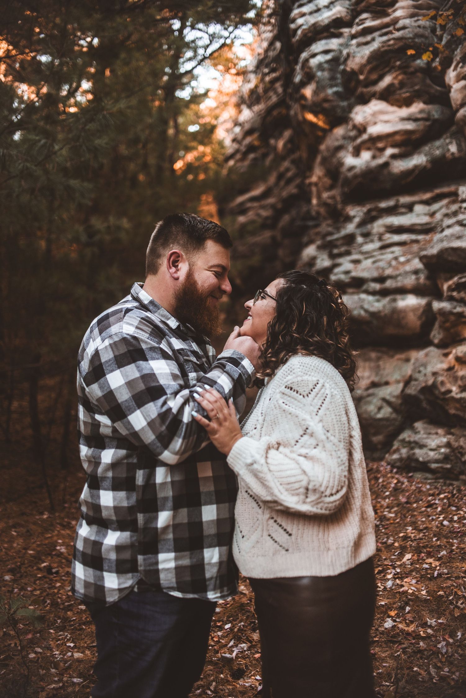 A couple shares an intimate moment against a rocky cliff backdrop in autumn.