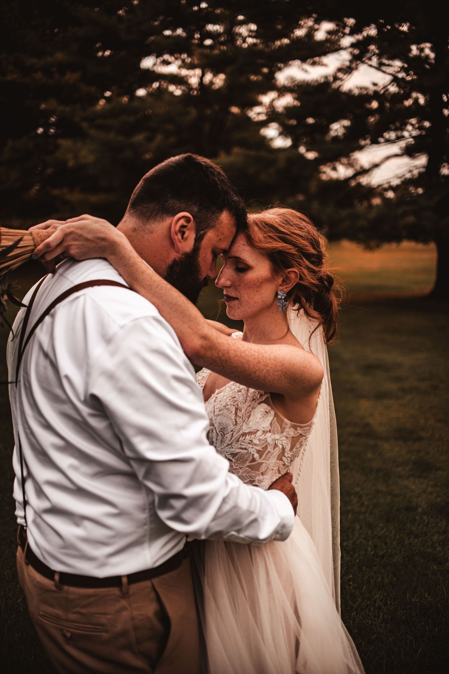 An intimate wedding portrait showing a tender embrace in a natural outdoor setting.