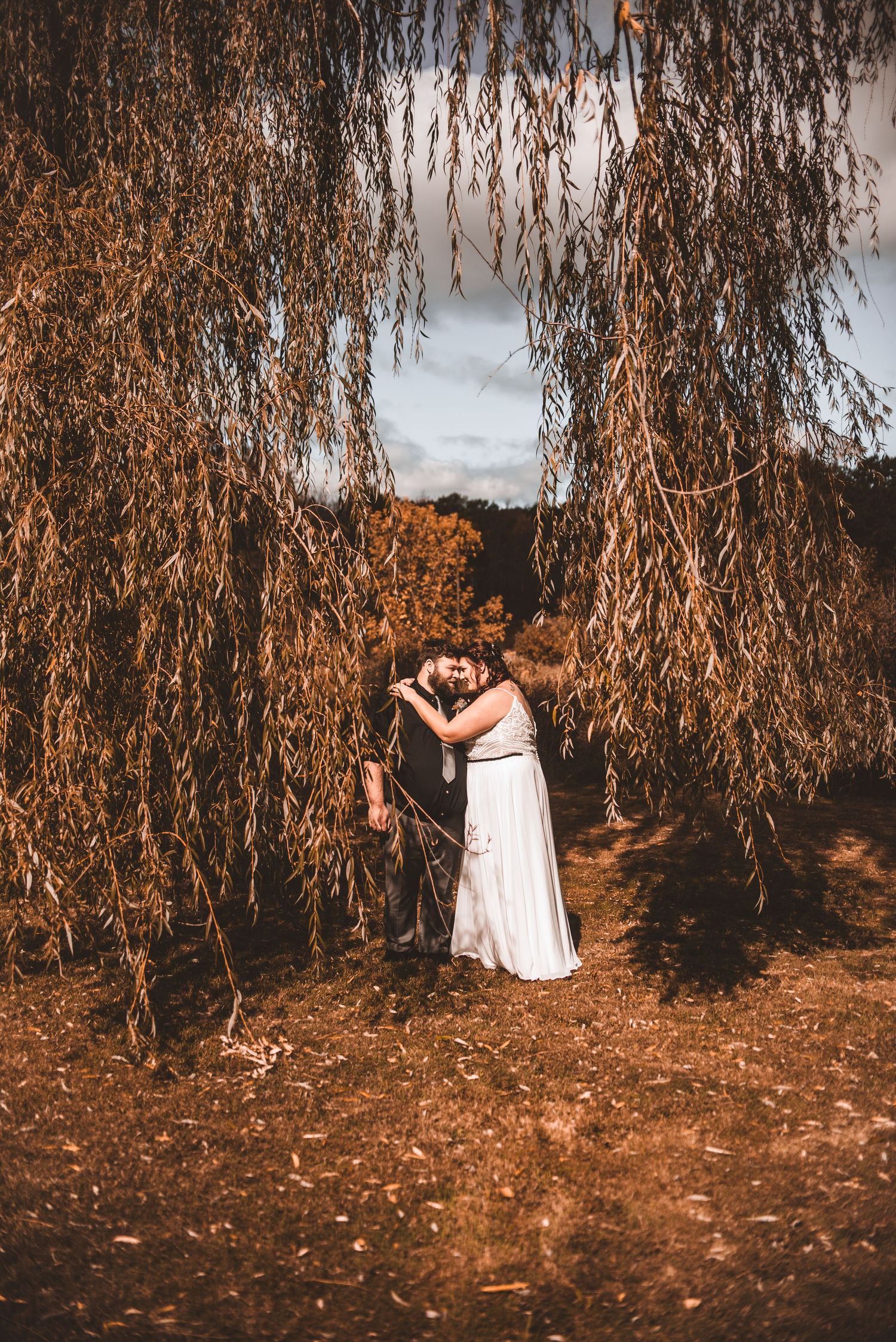 A romantic moment captured under a weeping willow tree with golden autumn light.