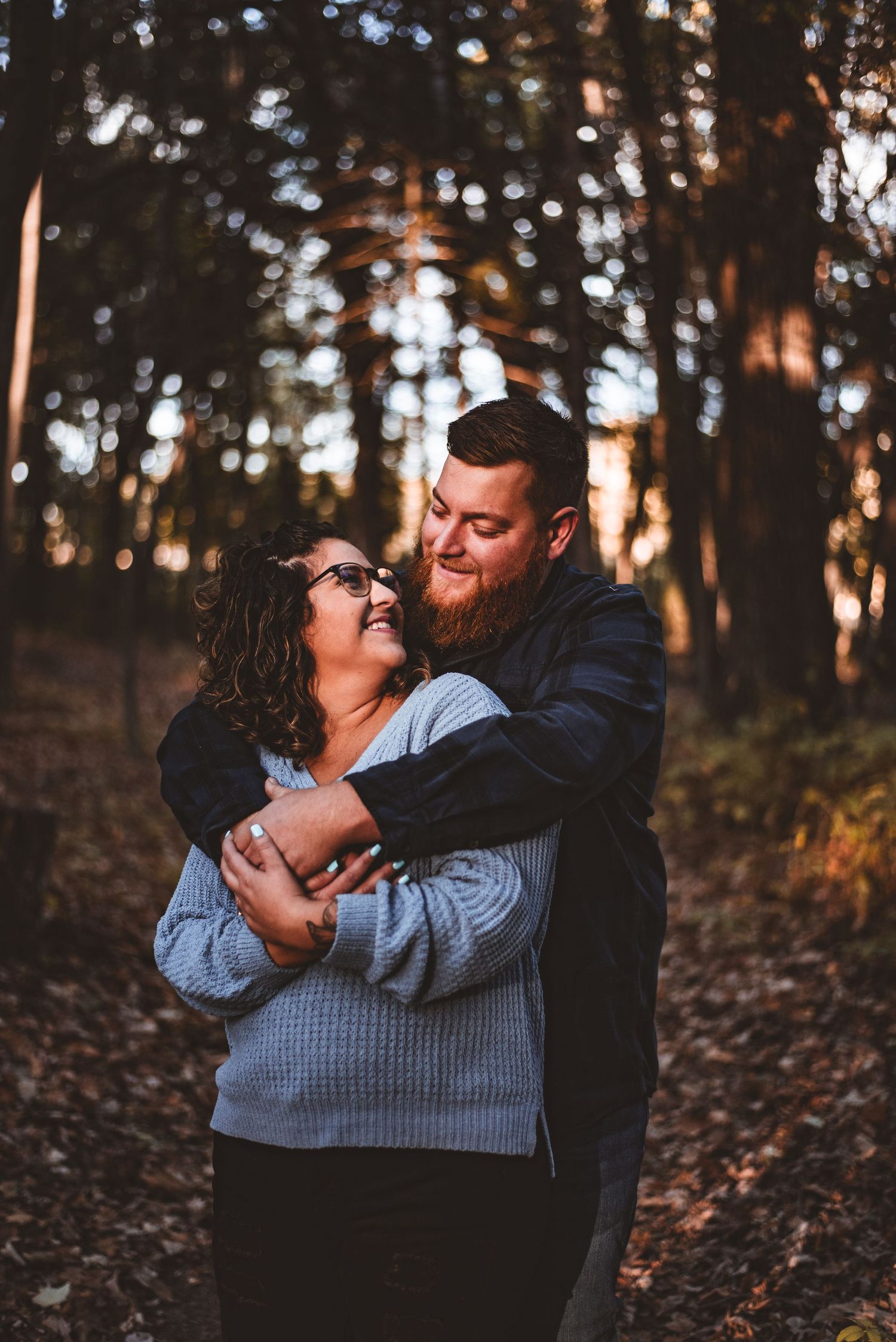 A joyful couple sharing laughter while embracing in a wooded setting at sunset.