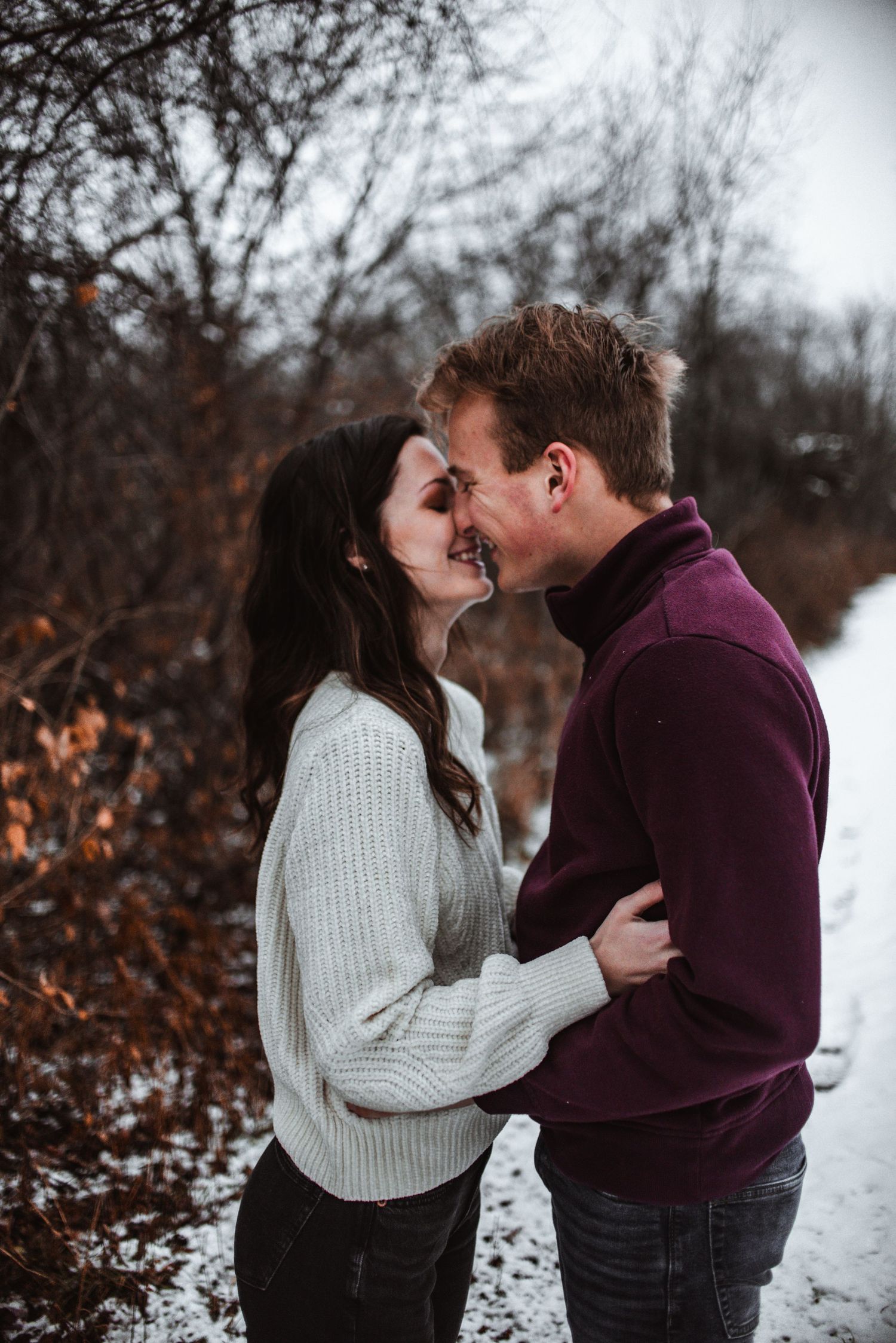 A tender winter engagement moment captured as a couple shares an intimate moment in the snow.