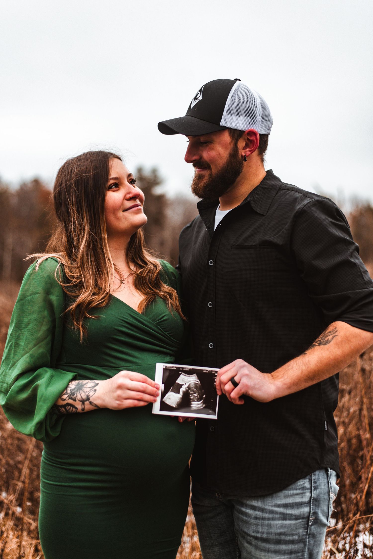 An expectant couple holding a sonogram photo while posing in a autumn field.