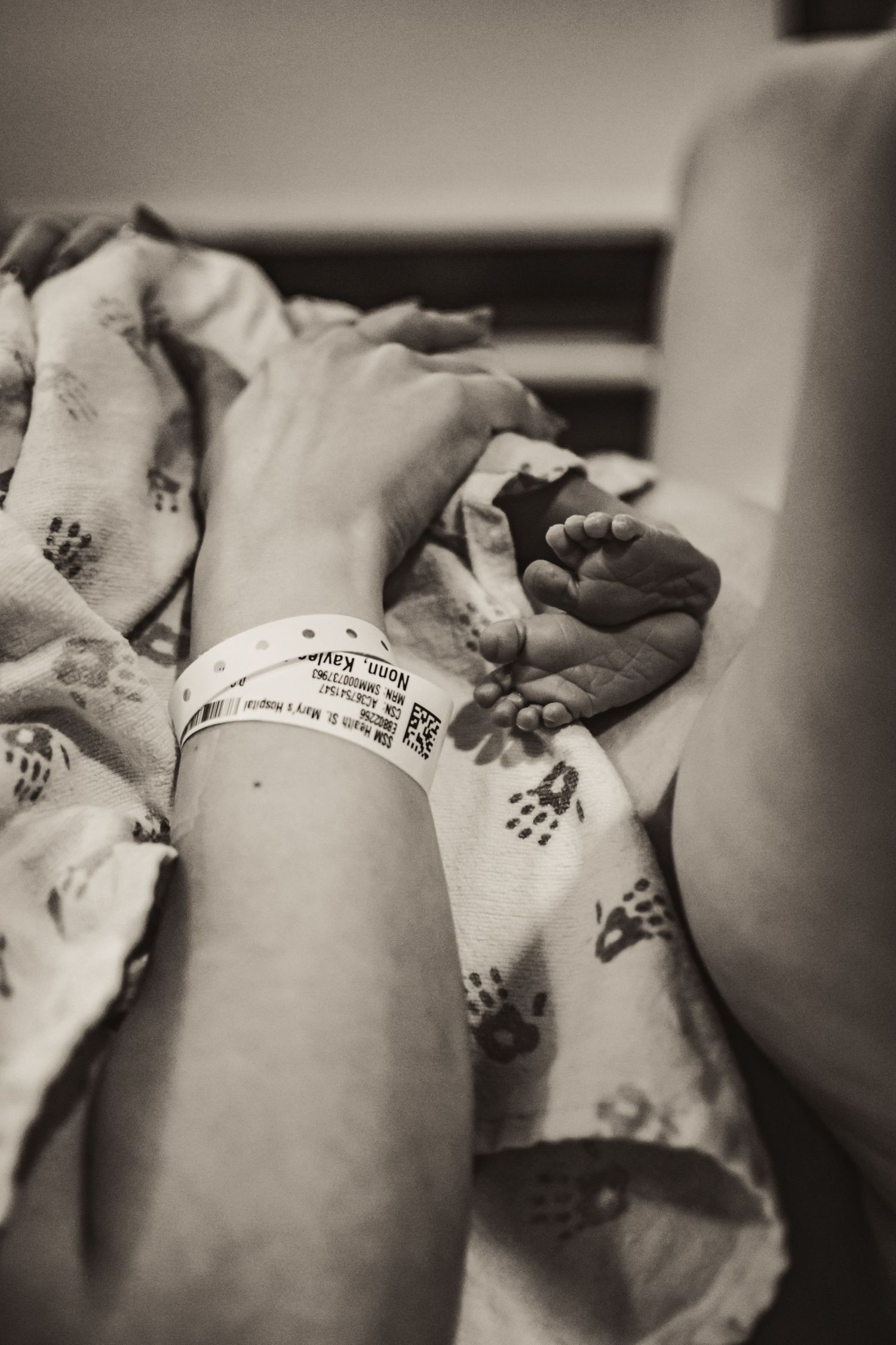Close-up black and white photo of a hospital bracelet and newborn baby's hand.