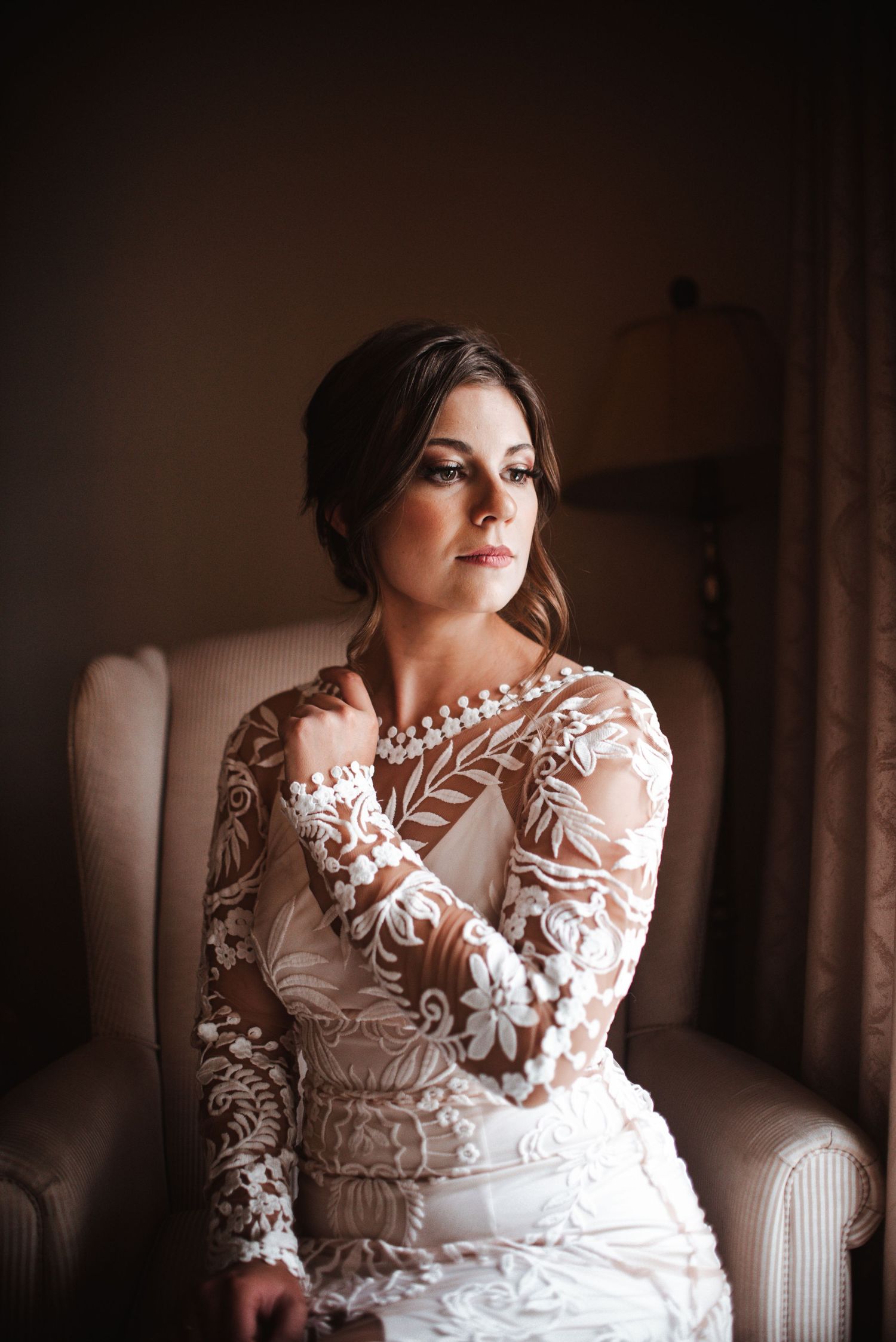Elegant lace wedding dress with intricate floral sleeve details photographed in moody natural lighting.