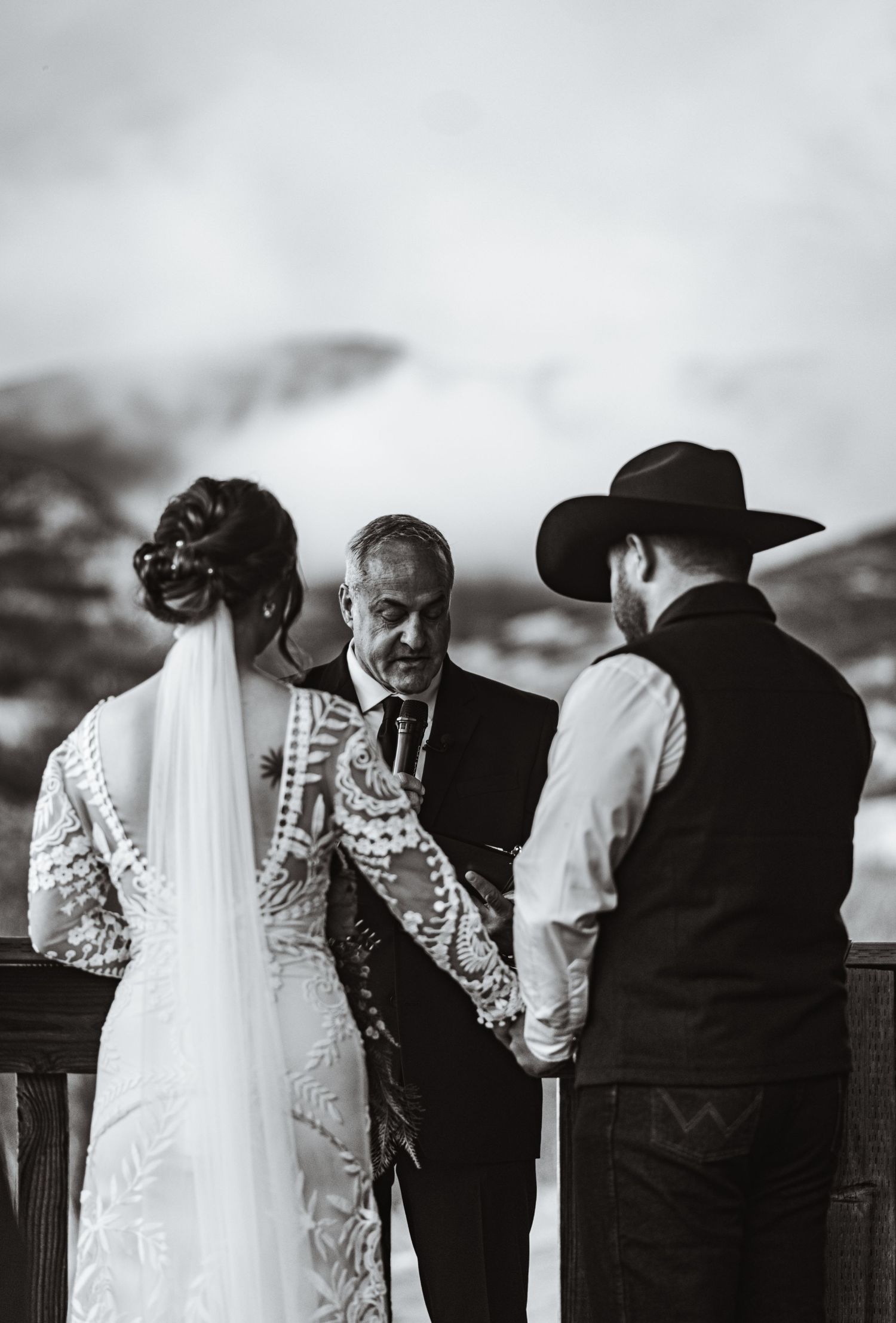 A black and white photograph captures an intimate outdoor wedding ceremony moment.