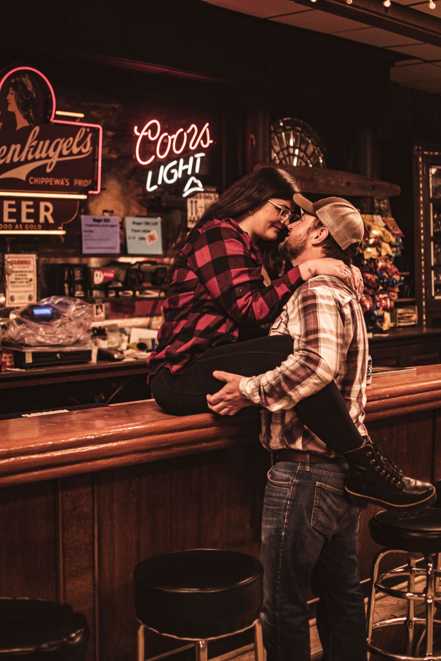Romantic scene in a dimly lit bar with neon beer signs glowing in the background.