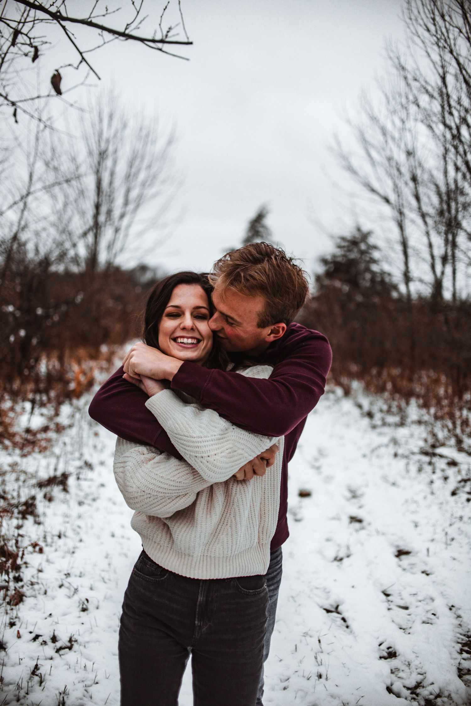 A loving winter engagement photo featuring a playful couple embracing in the snow.
