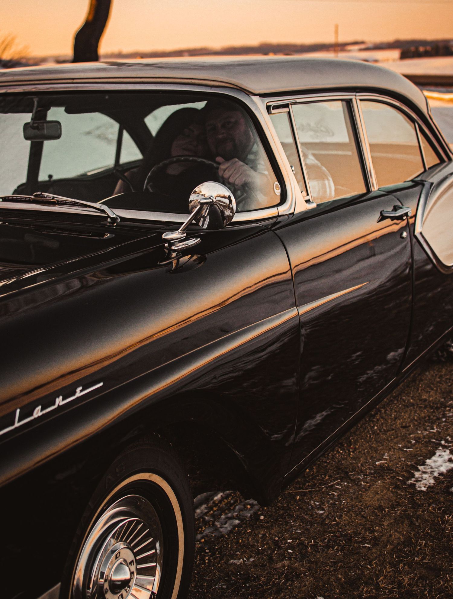 Classic black vintage car photographed at sunset with light reflecting off its sleek chrome details.